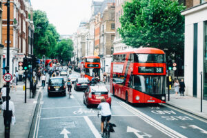 A busy street with red double decker buses, cars, taxis and a cyclist. 