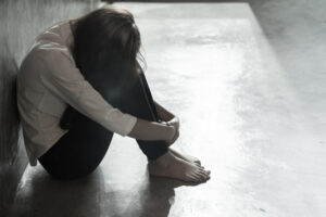 A woman sat on the floor with her head resting against her tucked up knees.