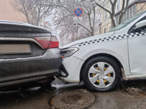 A taxi crashed into the side of a black car in icy/wintery weather. 