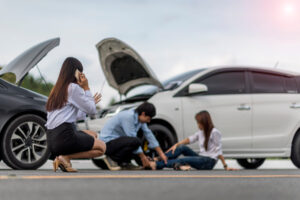 An uninsured driver calls an ambulance after a car collision, while a man in a blue shirt attends to an injured woman