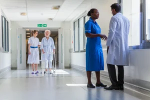 A doctor and nurse having a conversation in a hospital corridor as another nurse walks by with a patient