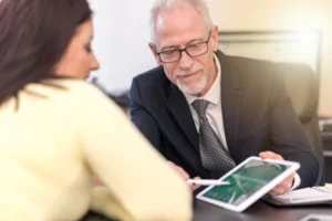 A No Win No Fee solicitor gesturing to a tablet while explaining medical negligence payouts to a claimant seeking compensation for a loved one's death