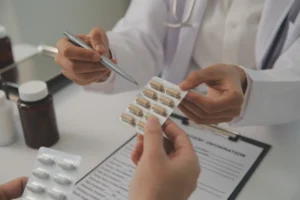 A healthcare professional issues medication in a blister pack to a patient over a desk with a checklist of side effects. 